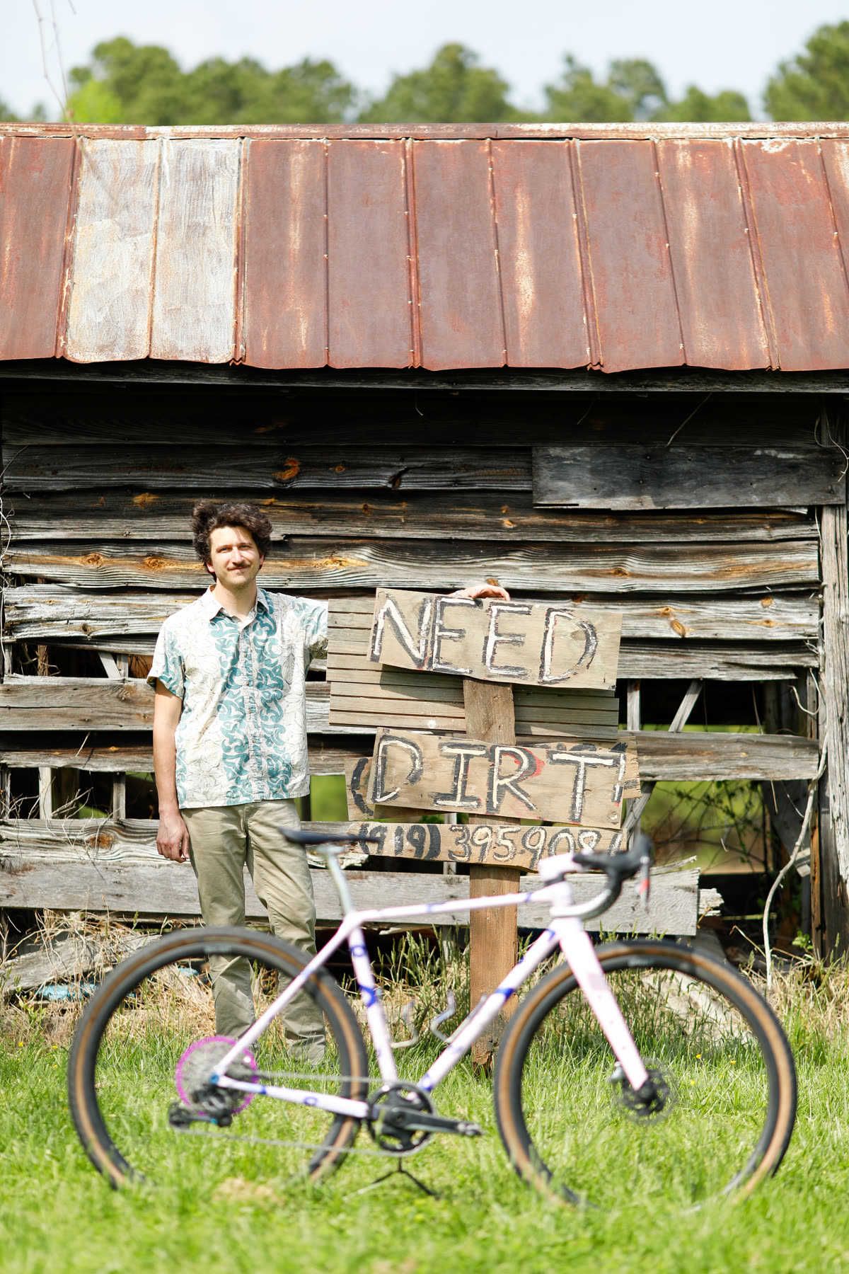 Dustin standing with the 401 in front of the barn and a Need Dirt sign - builder portrait