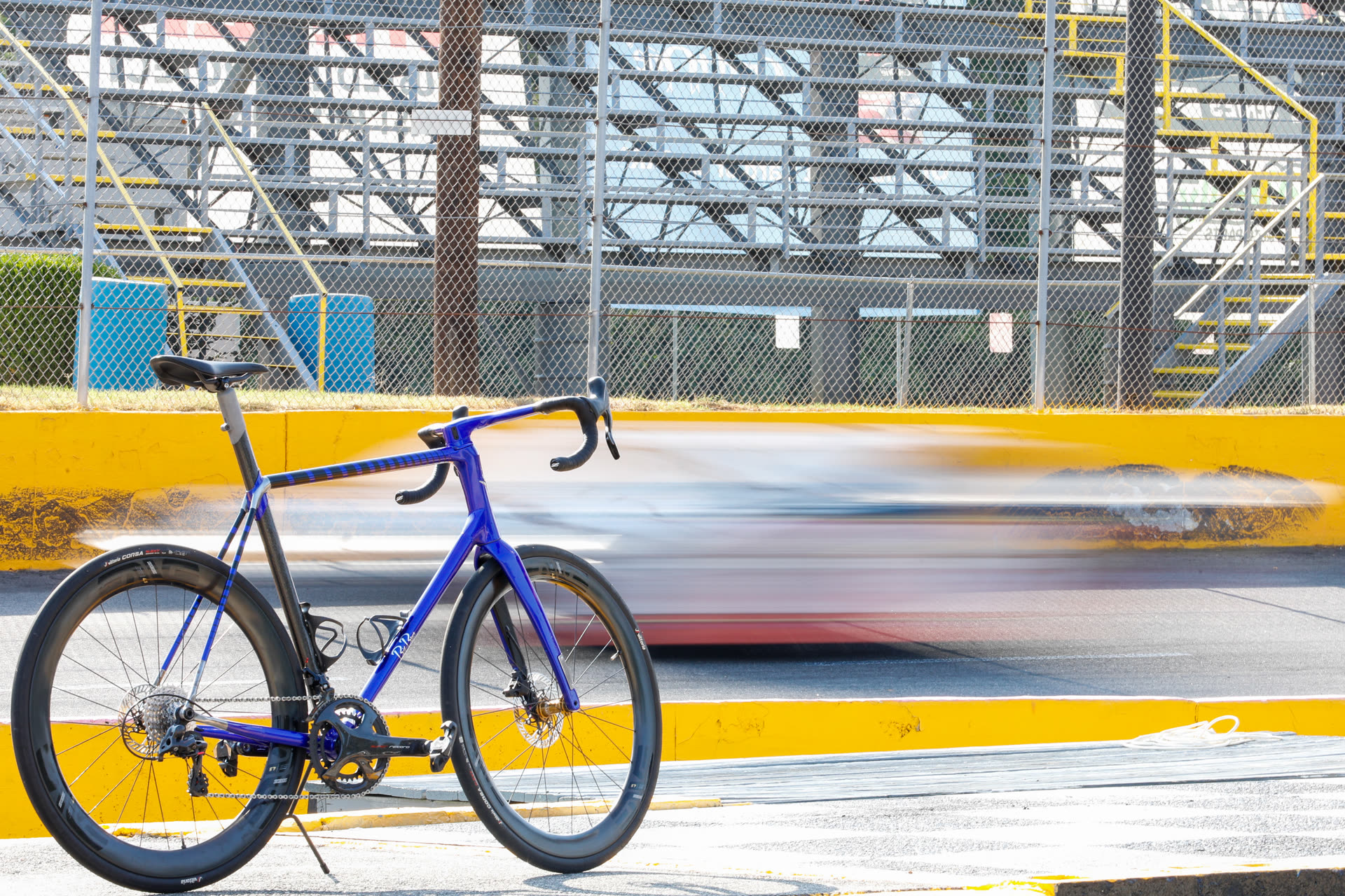 The 427 road bike in violet, parked trackside as a race car blurs past